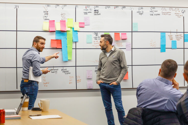 Two Skender team members reviewing a planning board covered with colorful sticky notes, discussing construction process improvements as part of their Lean approach.